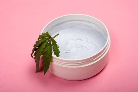 white round jar with a body scrub with a leaf of marijuana on a pink background close-up, cosmetics, skin care, beauty.の写真素材