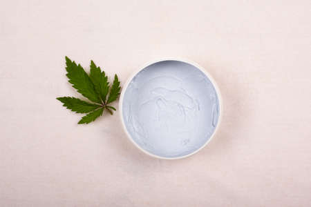white round jar with a body scrub with a leaf of marijuana on a white background top view, cosmetics, skin care, beauty.の写真素材