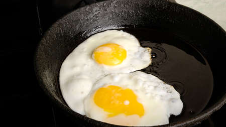chicken eggs, fried eggs in a cast iron pan close-up, breakfast, omelet, two eggs with yellow yolks...