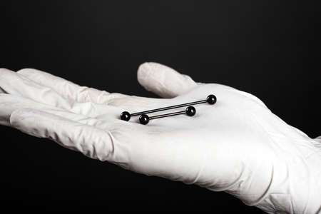 ear jewelry, piercing in hand with a disposable glove on a dark background.
