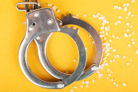 handcuffs and crystal drugs on yellow background, arrest of a drug dealer.の写真素材