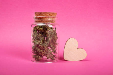 marijuana love symbol, jar with dry cannabis buds and a wooden heart on pink backgroundの写真素材