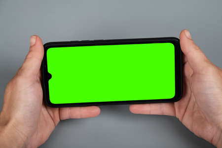 hands holding the phone horizontally, green chroma key mockup on smartphone