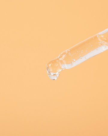 pipette with a drop of oil on a yellow background closeup