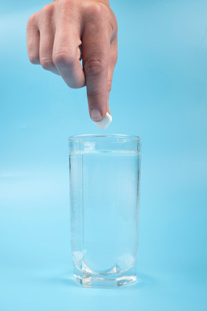 glass cup with water and a hand with a pill on blue background medication.の写真素材