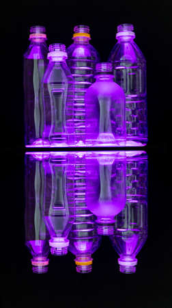 Illuminated clear recyclable plastic water bottles on black background with reflection. Pink lighting. Abstract fine art style depiction of consumer goods with neon like glow.の写真素材