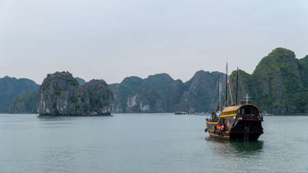 Cat Ba, Vietnam - November 19, 2019 : Junk boat cruising in Lan Ha Bay near Ha Long Bay, mountain...