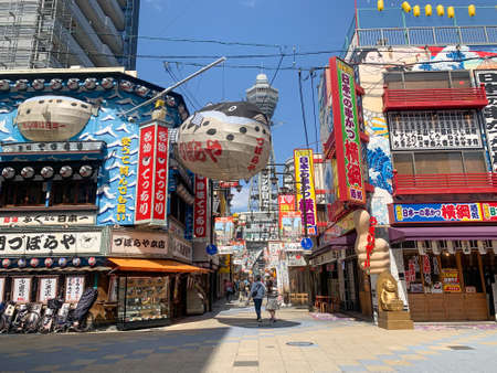 Osaka, Japan - April 5, 2020 : Asian man rides bike under large iconic puffer fish sign in Shinsekai district during Covid 19 pandemic. The associated fugu restarant Zuboraya has since closed down.のeditorial素材
