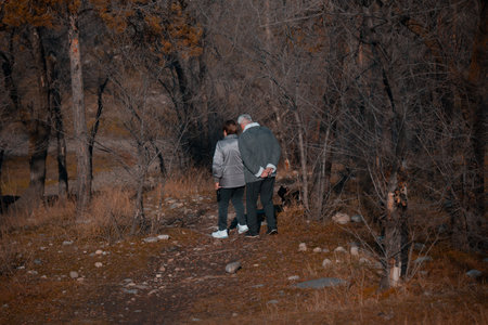 Back view of senior couple in love walking in autumn forest, looking at each otherの写真素材