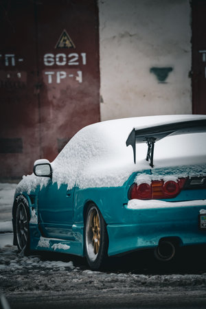 Old blue car covered with snow in the parking lot in winter.