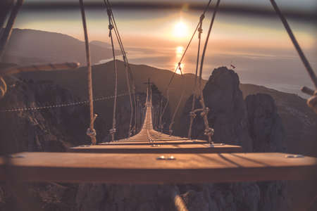 Rope ladder over abyss leading to a catholic cross during sunriseの写真素材