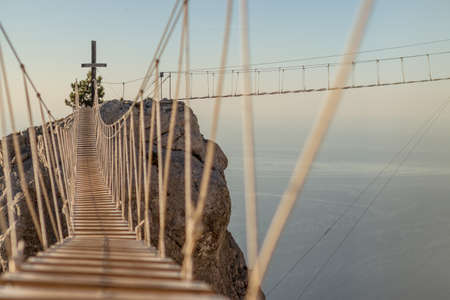 Two rope ladders over abyss leading to catholic cross standing on top of montainの写真素材