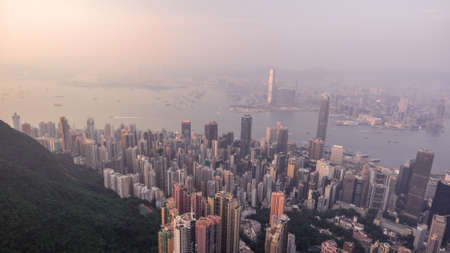 Beautiful aerial shot of many high skyscrapers covered with sunset fog or haze in Hong Kong, China. Top view of Victoria Harbour from Victoria Peak at sunset. City skyline.の写真素材