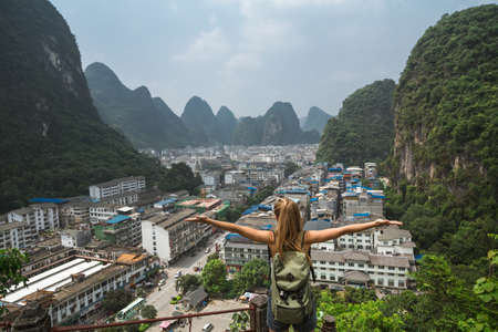 Rear view of girl with hands up looking at the karst mountain landscape and Yangshuo city vie in famous Guilin region, China. Love travelling, freedom, adventure and exploration concept.の写真素材
