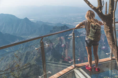View of young woman looking at the view from sky walk at Tianmen Mountain. It is a mountain located within Tianmen Mountain National Park, Zhangjiajie, in northwestern Hunan Province, China.の写真素材