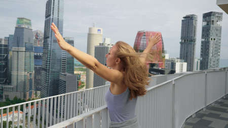 A happy tourist girl holds up her hands and enjoys the stunning view of the skyscrapers in Singapore on a warm summer day. Travel destination, adventure, success and exploration concept.の写真素材