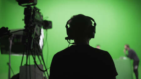 Film crew in green studio shooting video. Chroma - technology of combining two or more images or frames in single composition. Cameraman,director,crew. Filmmaking industry.の写真素材