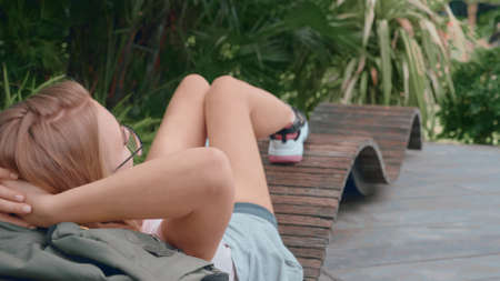 Relaxed young woman chilling on a bench outdoors in a tropical park. Recreation, leisure activity concept.の写真素材