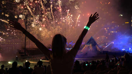 Firework streaks in night sky, celebration background. Silhouette of a young woman against illuminated sky.の写真素材