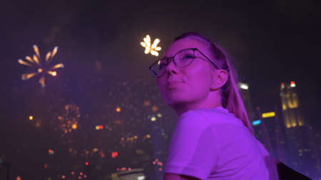 Young happy woman enjoying fireworks in the night sky on New Years Eve in Singapore. Nightlife, party or open air. Leisure activity, entertainment, Christmas celebration concept.の写真素材