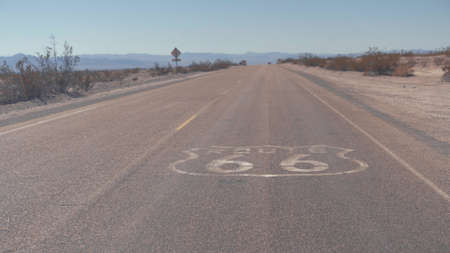 Route 66 road sign. Historic street with nobody. Classic concept for travel and adventure in a vintage way. Street sign on historic route 66 in the Mojave desert photographed against the sun at sunsetの写真素材