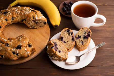 Banana cake with blueberries and cereal. Laid out on a Board with a tea set, bananas and blueberries on wooden tableの写真素材