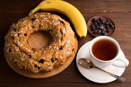 Banana cake with blueberries and cereal. Laid out on a Board with a tea set, bananas and blueberries on wooden tableの写真素材