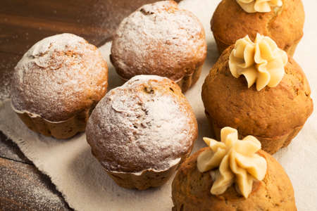 Sweet, lush cupcakes with cream and dusted with powdered sugar. On white fabric and wooden tableの写真素材