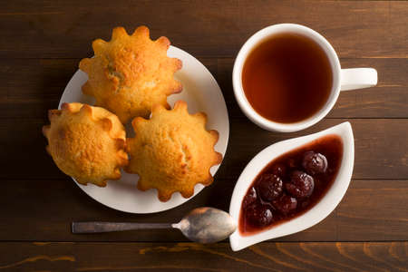 Sweet lush cupcake with strawberry jam and tea. In white dish on wooden tableの写真素材
