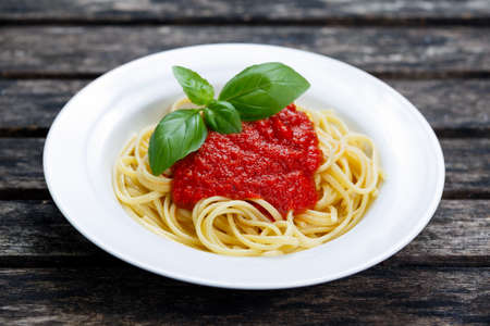 Spaghetti with marinara sauce and basil leaves on top, on wooden tableの写真素材