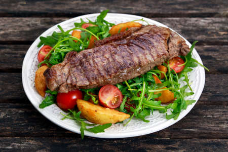 rare beef steak with roasted potatoes, tomatoes and wild rocket leaves. on old wooden table.の写真素材