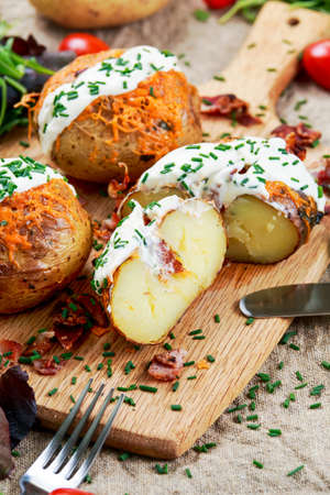 Hot Baked Potato with cheese, bacon, chives and sour cream on cutting board.の写真素材