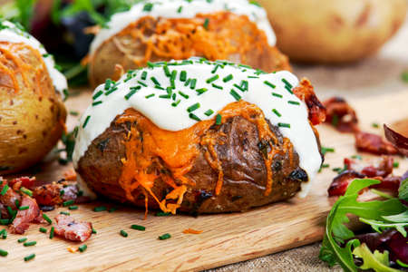 Hot Baked Potato with cheese, bacon, chives and sour cream. on cutting boardの写真素材