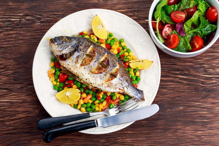 Sea bream baked with herbs and lemon. with vegetable mix. on plate.の写真素材