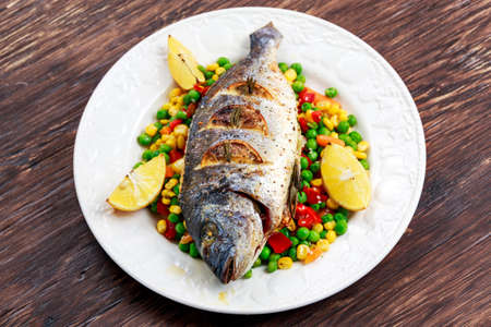 Sea bream baked with herbs and lemon. with vegetable mix. on plate.の写真素材