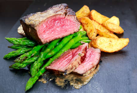 Beef steak Mignon cooked with Asparagus, potatoes, garlic and tomatoes. Served on blue stone board.の写真素材