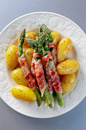 Bacon Wrapped Asparagus with young potato on plate.の写真素材