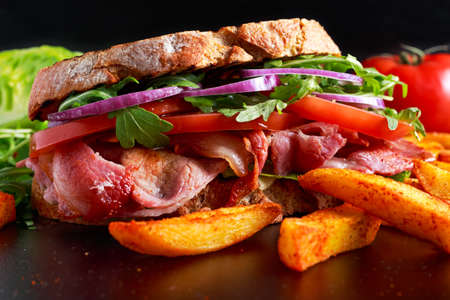 Fresh homemade BLT sandwich on grilled bread with bacon, lettuce, beef tomato, red onions, wild rocket and chips.の写真素材