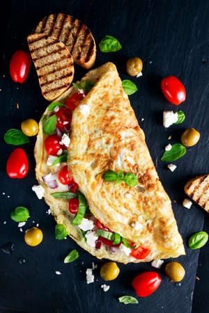 Vegetables Omelette with tomatoes, basil, greek cheese, parmesan, olives, grilled toast on stone boardの写真素材