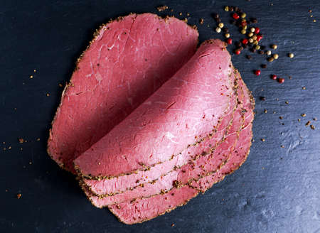 Peppered roast beef pastrami slices on paper with grains of coloured pepperの写真素材
