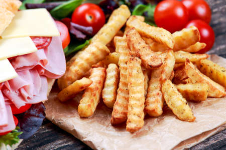 Fried Potatoes and Sandwich with lettuce, slices of fresh tomatoes, salami, hum and cheeseの写真素材