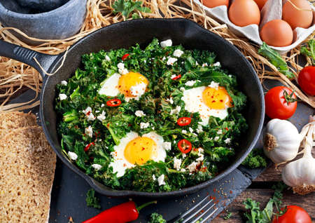 Homemade Green Kale with eggs, feta cheese, herbs, chili in iron pan. healthy rustic breakfast.