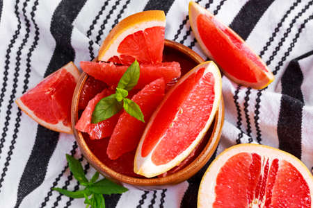 Juicy grapefruit Pilled pieces in wooden bowl with fresh mint lieves and slicesの写真素材