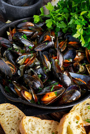 Boiled mussels in iron pan cooking dish. with herbs, butter, lime, parsley, garlic and fresh bread