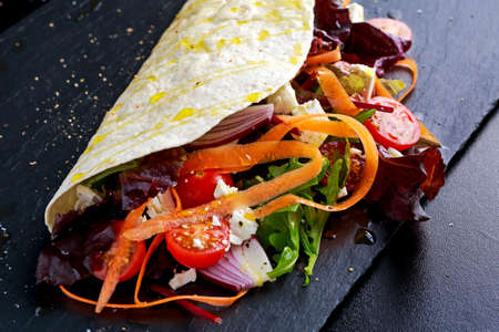Vegetarian tortillas taco wrap with red onion, sweet cherry tomatoes, carrots, ruby red chard, rocket and feta chees drizzled with olive oil.の写真素材