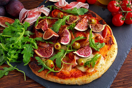 Fig pizza with bacon, green pimiento olives, rocket and basil leaves.の写真素材