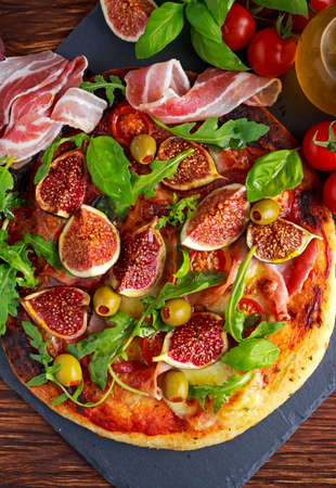 Fig pizza with bacon, green pimiento olives, rocket and basil leaves.の写真素材