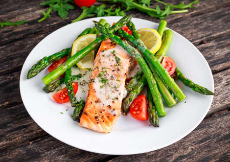 Fried salmon with asparagus, tomatoes, lemon, yellow lime on white plate.の写真素材