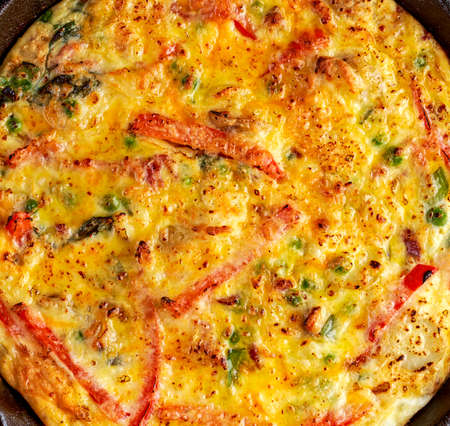 Frittata made of eggs, potato, bacon, paprika, parsley, green peas, onion, cheese in iron pan on wooden tableの写真素材