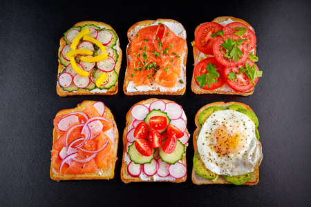 Variety of vegetarian toast sandwiches with salmon, raddish, tomatoes, cucumber, avocado,fried egg and sweet pepper.の写真素材